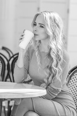 beautiful young girl drinks coffee from a cardboard cup in a cafe with wicker furniture