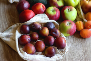 Straw bag and reusable fabric bags filled with various healthy fruit and vegetables. Wooden background, selective focus.