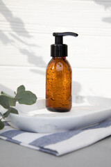 Amber bottle with facial cosmetics on a tray with a branch of eucalyptus on the gray wooden...