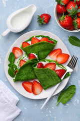 Spinach green crepes or pancakes with ricotta and strawberries on a plate for breakfast. Healthy dessert. Top view