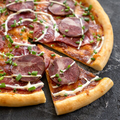 Pizza with cheese, sausage and green onions cut into pieces. Italian Cuisine. Dark gray background. Close-up. View from above. Copy space. Soft focus. 