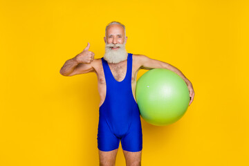 Portrait photo of old age grandfather handsome gray hair bearded showing thumb up like recommend hold fitness ball isolated on yellow color background