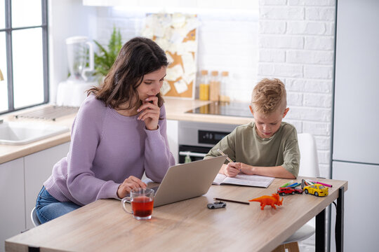 Work From Home And Family Education, Mom And Son Using Remote Access Technology For Learning And Work, Woman Works On Laptop, Child Writes In Textbook