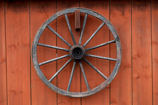 old wooden wagon wheel hanging on a red barn wall