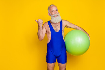 Portrait photo old age grandfather sportive body muscular hold fitball finger point empty space advert recommend ad isolated on yellow color background