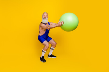 Full length photo of cheerful man professional fitness coach doing squats preparing cross marathon isolated on yellow color background