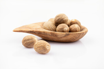 Nutmeg in a wooden olive bowl and whole seeds on a white background