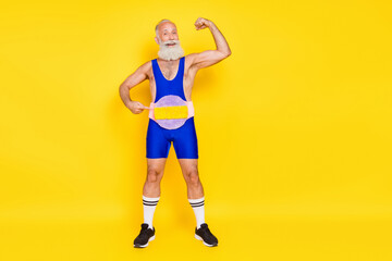Fototapeta na wymiar Photo of sportive confident man pensioner dressed blue overall triumph belt showing biceps empty space isolated yellow color background