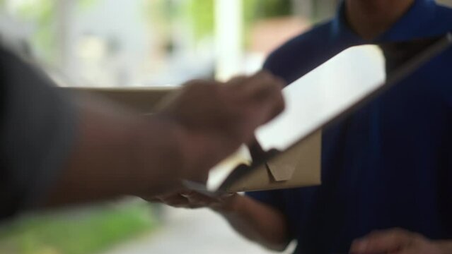 Hand man signing electronic Signature on tablet for agreement of contract digital receiving parcel from blue delivery man from shopping online. Courier man delivering package to destination.