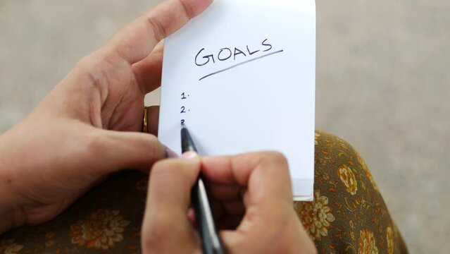  women hand writing new year goals on notepad on table 