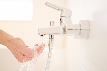 Male hand checking the temperature of flowing water from a faucet in a bright bathroom