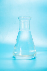 clear liquid with water bubbles in a glass laboratoryy flask, bottle isoalted over blue background
