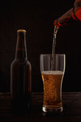 A stream of beer from the bottle pours into the beer glass, causing a lot of bubbles and foam.