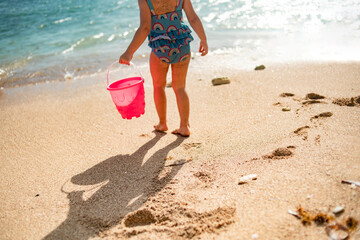 Adorable little girl playing with sand on the beach and having fun with toys of
beach and swimsuit on sunny day