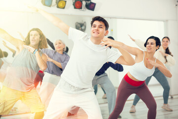 Cheerful sporty young guy practicing modern vigorous dance movements in group dance class ..