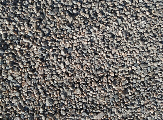 Small granite stones lie on a dirt road, top view in the rays of the midday sun.