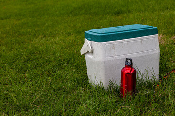 White cooler box with green lid and a red water bottle on a green lawn