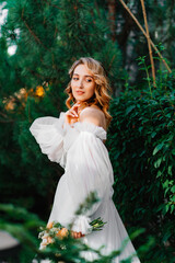 a bride in an open-shouldered dress poses against the backdrop of greenery