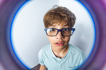 An exaggerated close up portrait of a funny little boy with glasses making a thinking face