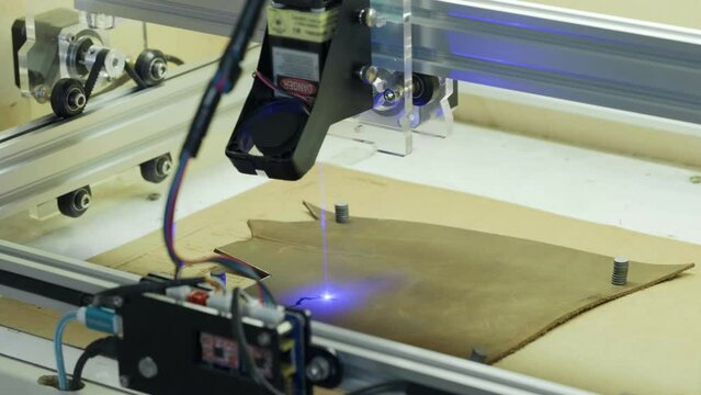 Laser burning on eco leather. Cropped view of the laser machine burning on leather at workshop. laser beam making logo or design on material. Bag manufacturing 
