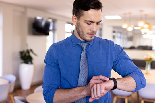 Caucasian businessman wearing blue shirt using his smartwatch in modern office