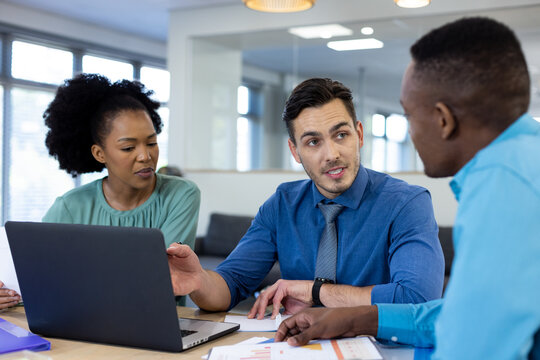 Happy diverse business people using laptop and discussing in modern office