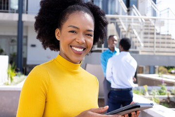 Portrait of happy african american businesswoman using tablet with diverse colleagues in background