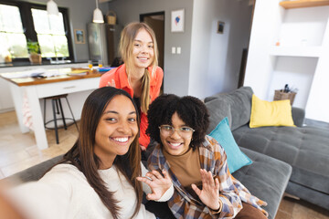 Portrait of happy diverse teenage female friends sitting on couch taking selfie