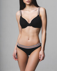 Fototapeta premium The body of a slim young girl in sexy lingerie on a studio gray background. Diet, fitness, healthy lifestyle
