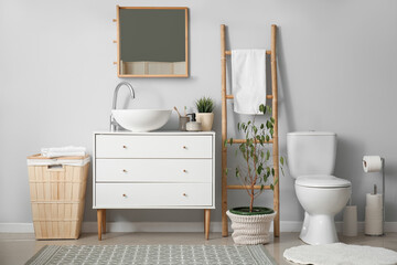 Interior of light bathroom with drawers, toilet bowl and laundry basket