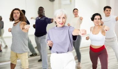 Foto op Plexiglas Portrait of smiling determined elderly woman practicing basic punches during group self defense course © JackF