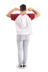 Young man suffering from loud noise on white background, back view