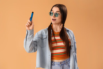 Young woman in sunglasses with disposable electronic cigarette on beige background