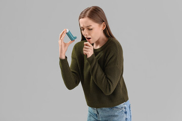 Sick young woman with inhaler on grey background