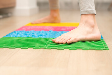 People. Healthy lifestyle. a teenager boy stands on a multi-colored orthopedic massage mat with bare feet.