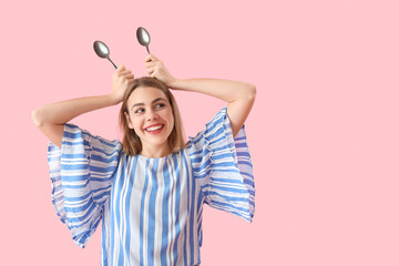 Funny young woman with spoons on pink background