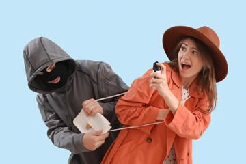 Young woman with pepper spray defending herself against thief on blue background