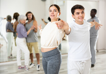 Positive young girl and guy dancing in couple during group class in choreography studio, enjoying slow elegant waltz