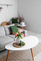Vase with tulips and Easter rabbits on table in living room