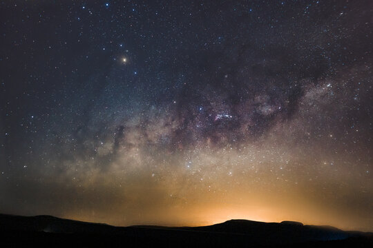 Photo of the milky way with light pollution and mountains in the foreground with many stars in the sky and artistic colors.
