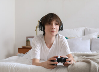 Teenage boy with headphones playing video game in bedroom