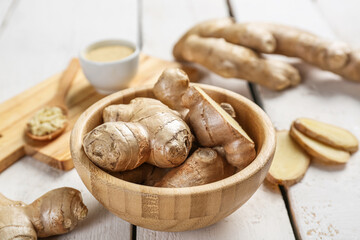 Wooden plate with ginger roots on light wooden background