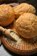 Board with delicious fresh buns and scoop of sesame seeds on black wooden table