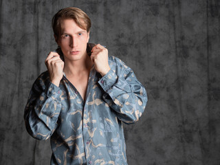 Stylish elegant young man in a blue silk shirt posing in the studio on a gray fabric background