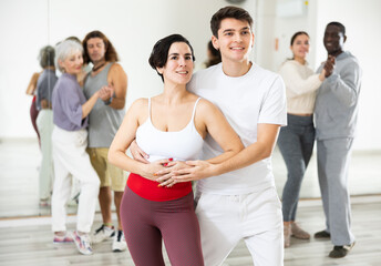 Smiling young Hispanic woman and handsome guy attending group choreography class, learning modern...