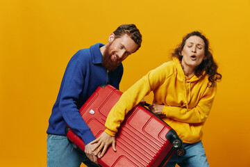Obraz premium Woman and man smiling, suitcases in hand with yellow and red suitcase smiling merrily and crooked, yellow background, going on a trip, family vacation trip, newlyweds.