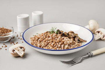 Plate of tasty buckwheat porridge with mushrooms and dill on grey background