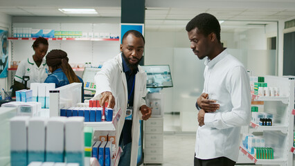 Young man with stomachache asking pharmacist for pills, being in pain and talking to specialist...