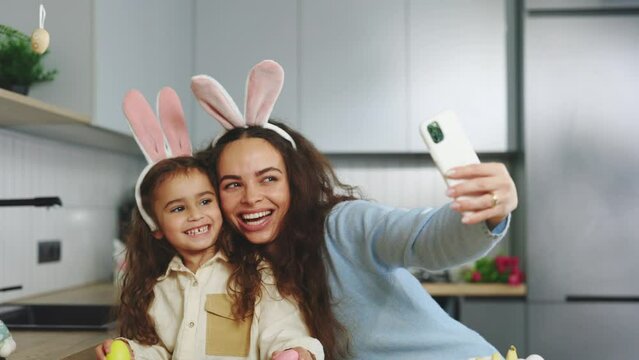 Smiling Mother and Daughter Selfie with Easter Eggs, Wearing Bunny Ears, Beauty and Fun Day Together at Home. Happy Easter. Concept of Childhood, Technology, Family's Weekend