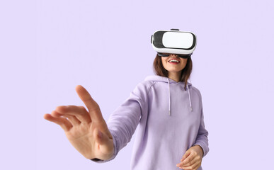 Pretty young woman in VR glasses on lilac background